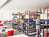 Two female students look for books in a library