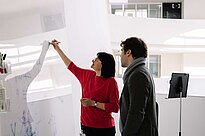 Two people standing in front of a whiteboard writing on it