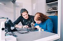 Eine Studentin arbeitet an einer Maschine, während ein Student zusieht