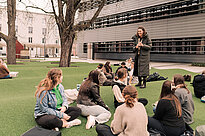 Eine Gruppe von Studenten sitzt im Gras auf dem THA-Campus und hört einem stehenden Studenten zu.