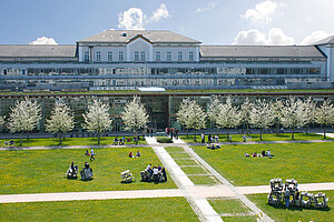 @ OTH Amberg-Weiden A university building surrounded by a green lawn and blossoming trees.