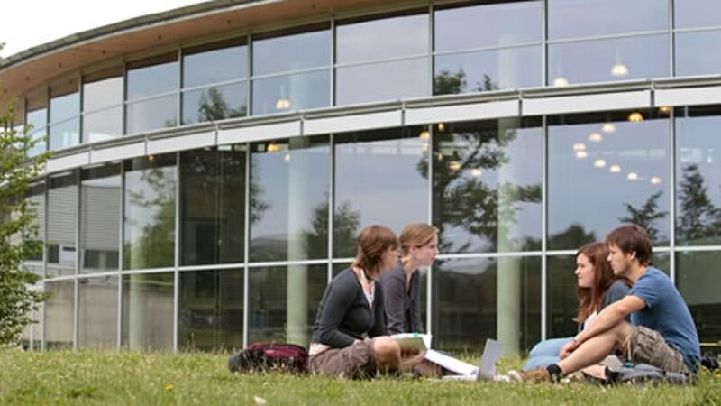 Four students sitting in front of a University Building