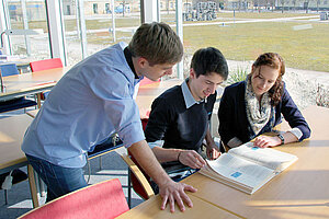 @ OTH Amberg-Weiden Three students looking at a book in a library.