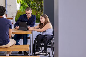 A male student and a female student in wheelchairs look at a laptop together.