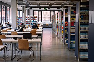 Facilities of the Library in Erlangen @Anna Tiessen A modern library with many vacant seats on the left and shelves of books on the right. The room is spacey with big windows.