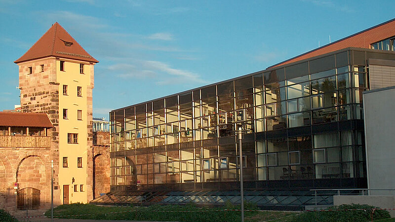 @ FAU A modern building with glass window next to an old medieval tower.