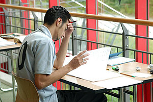 @ Uni Bayreuth A student flips a book with one hand and puts the other hand on the forehead