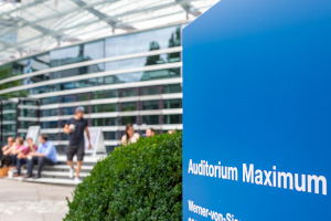 @ TUM Das Hochschulgebäude und ein Schild "Auditorium Maximum" im Vordergrund