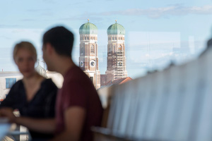 @ TUM Studierende auf der Terrasse eines Hochschulgebäudes, im Hintergrund die Frauenkirche