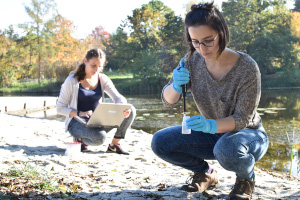 @ Uni Bayreuth Two women working on the bank of a lake: one taking samples and the other using a computer